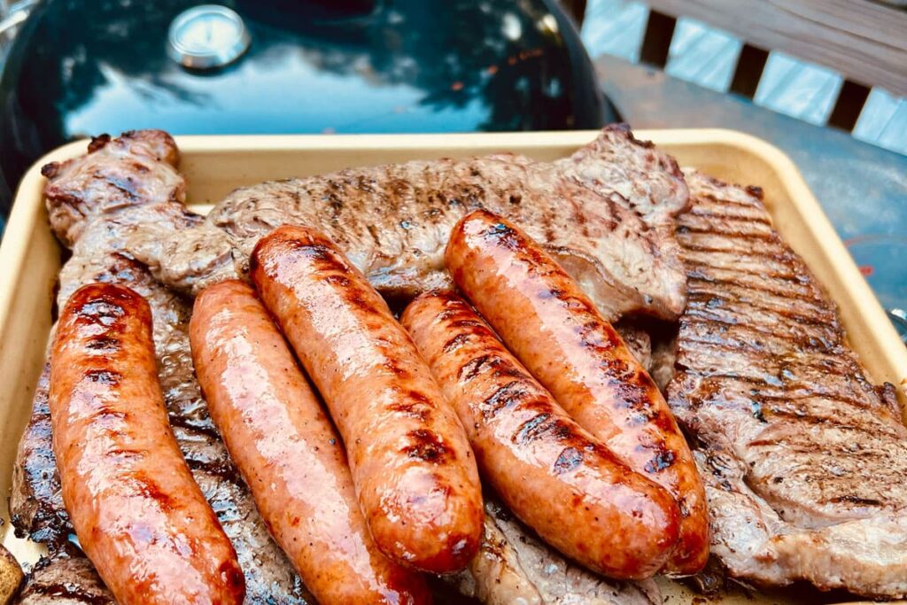 grilled brats and strip steaks resting on a tray